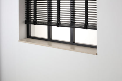 Beige composiet vensterbank Sinaj Pearl met honed afwerking onder een zwart raam met jaloezieën.