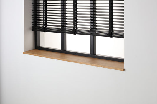 Eiken gefineerde vensterbank met matte blanke lak onder een zwart raam met jaloezieën.